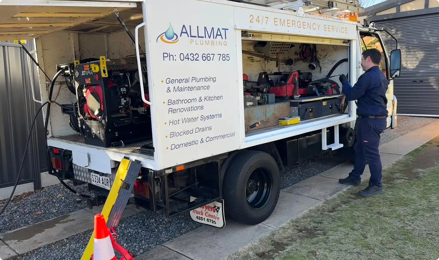 The Allmat Plumbing Isuzu service truck with its rear roller door open, a Jetwave drain jetter on the tray and the body signed 24/7 Emergency Service.